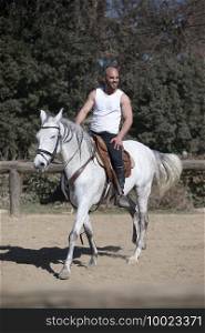 Young man in casual outfit riding white horse on sandy ground