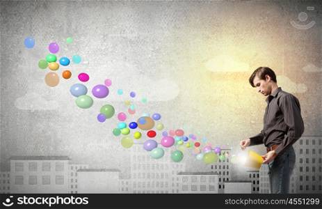 Young man in casual splashing colorful balloons from bucket