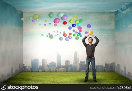 Young man in casual splashing colorful balloons from bucket