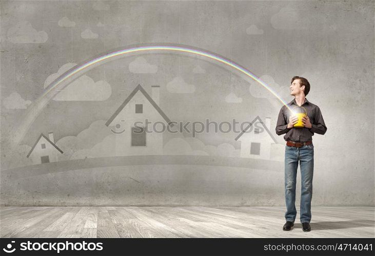 Young man in casual splashing rainbow from bucket