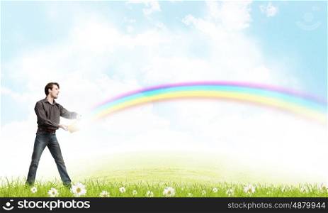 Young man in casual splashing rainbow from bucket