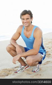 Young Man In Fitness Clothing Resting After Exercise On Beach