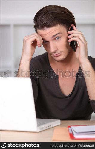 Young man in front of computer on the phone