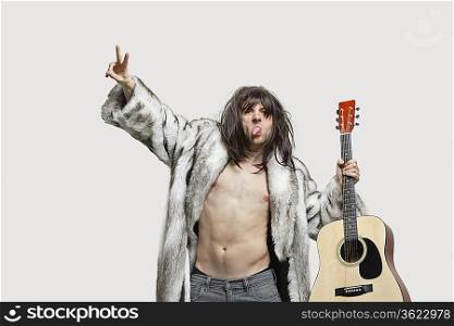 Young man in fur coat holding guitar while gesturing over gray background
