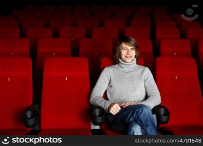 Young man in grey sweater sitting in the cinema alone