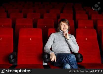 Young man in grey sweater sitting in the cinema alone