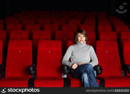 Young man in grey sweater sitting in the cinema alone