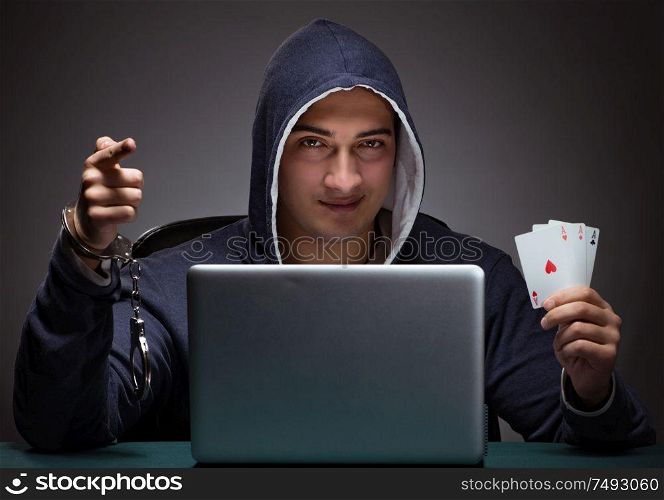Young man in handcuffs wearing a hoodie sitting in front of a laptop computer gambling. Young man in handcuffs wearing a hoodie sitting in front of a la