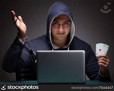 Young man in handcuffs wearing a hoodie sitting in front of a laptop computer gambling. Young man in handcuffs wearing a hoodie sitting in front of a la