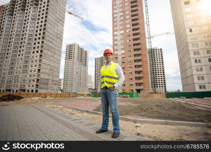 Young man in hardhat and safety vest standing on building site