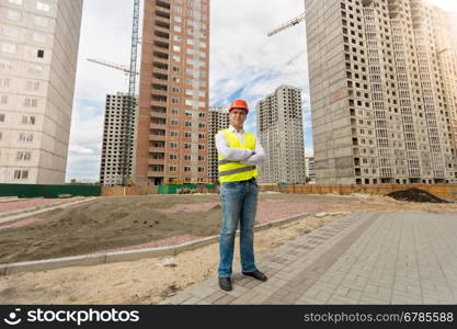 Young man in helmet and safety vest standing on building site
