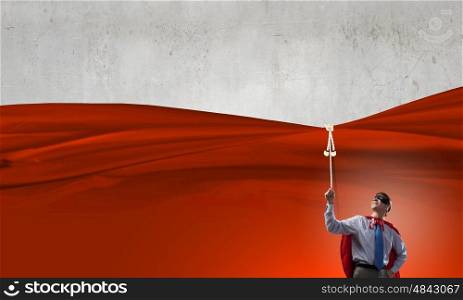 Young man in hero costume pulling blank banner from above. Place for your text