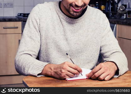 Young man in kitchen is writing notes