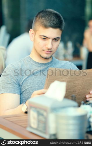 Young man in outdoor restaurant looking at the menu