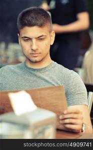 Young man in outdoor restaurant looking at the menu