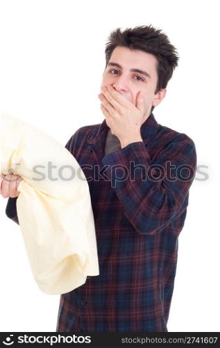 young man in pajamas yawning and holding pillow isolated on white background