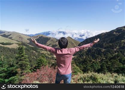 Young man in pink long sleeved t-shirt enjoying the amazing view on top of mountain