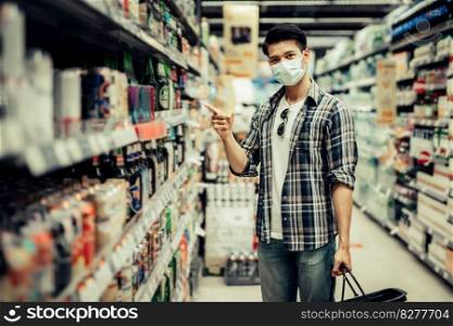 Young man in protective mask holding basket and stand in beverage section and point on alcohol beverage bottle, New normal lifestyle and shopping concept