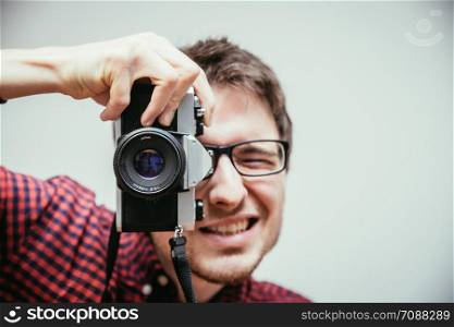 Young man in red-blue checked shirt is taking a picture with an vintage camera, retro style