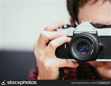 Young man in red-blue checked shirt is taking a picture with an vintage camera, retro style