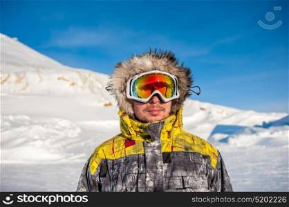 Young man in ski goggles outdoors with French Alps covered with snow at background. Val-d&rsquo;Isere, France