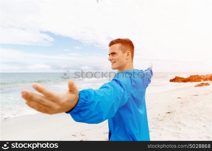 Young man in sport wear with outstretched arms. Young man in sport wear with outstretched arms standing on beach