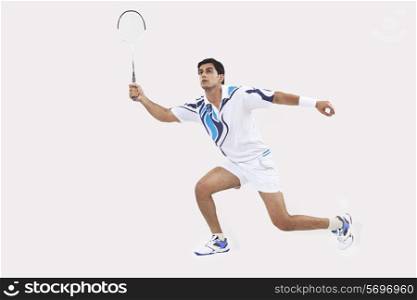 Young man in sports wear playing badminton against white background