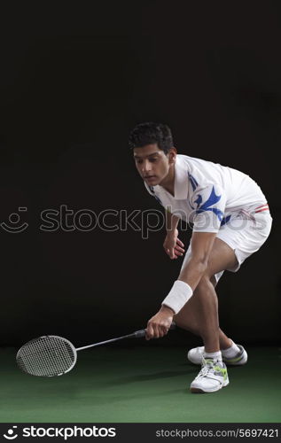 Young man in sportswear playing badminton over black background