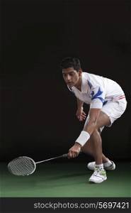 Young man in sportswear playing badminton over black background