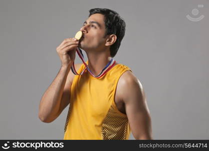 Young man in spots wear kissing gold medal isolated over gray background