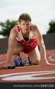 Young man in starting blocks holding relay baton, portrait