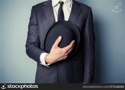 Young man in suit is holding a bowler hat