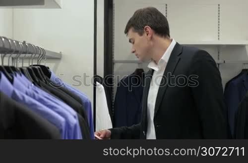 Young man in suit is looking price labels in menswear store.