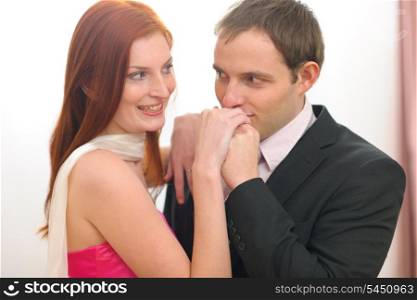 Young man in suit kissing hands of red hair woman in evening dress