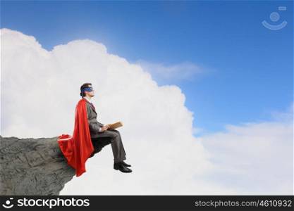 Young man in super hero costume sitting with book in hands. Bored superhero