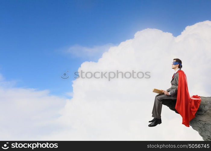 Young man in super hero costume sitting with book in hands. Bored superhero