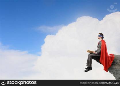 Young man in super hero costume sitting with book in hands. Bored superhero