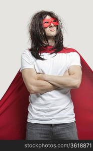 Young man in super hero costume standing with arms crossed against gray background