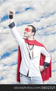 Young man in superhero costume with hand raised against cloudy sky