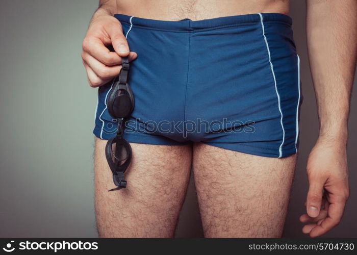 Young man in swimming trunks with goggles in his hand