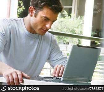 young man in t-shirt sitting on sofa at home, working on laptop computer