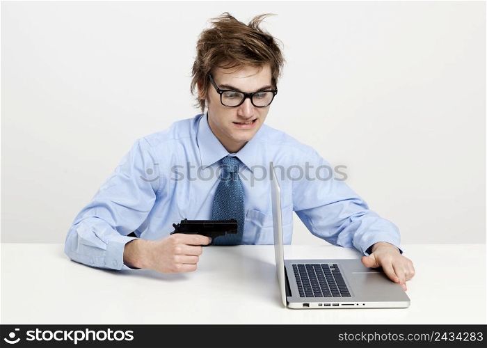 Young man in the office and pointing a gun to the laptop