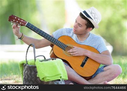 young man in the park tuning his guitar