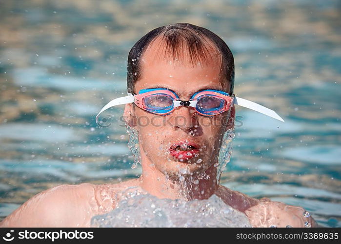 young man in watersport goggles swimming in pool, Aome up from water