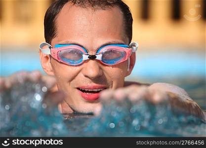 young man in watersport goggles swimming in pool, extended hands forward