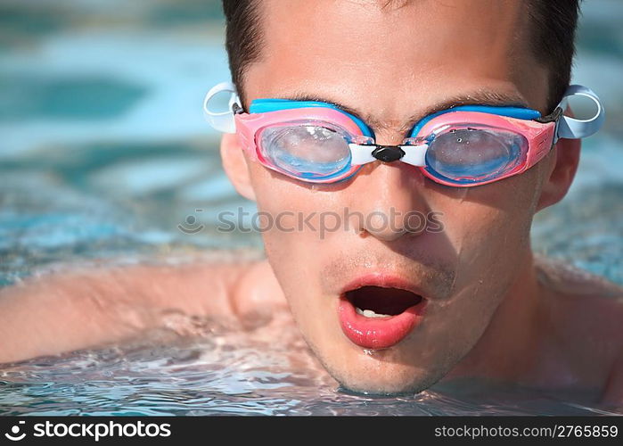 young man in watersport goggles swimming in pool, taking breath