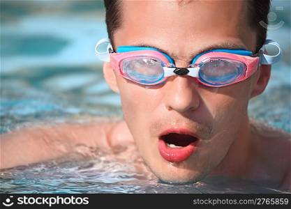 young man in watersport goggles swimming in pool, taking breath