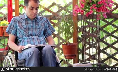 Young man in wheelchair reading outdoors