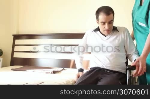 Young man in wheelchair transfering in bed with nurse help.