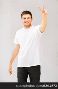 young man in white blank t-shirt showing victory or peace sign